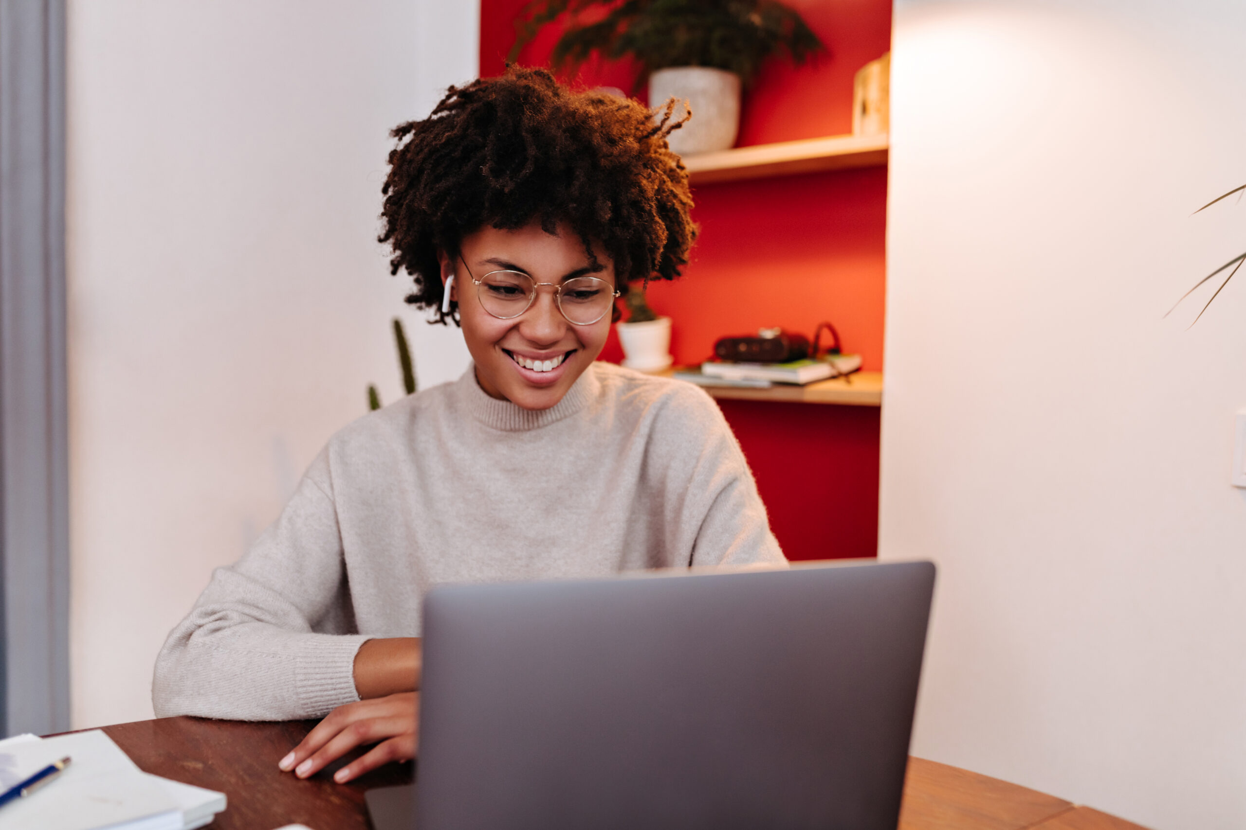 Woman in wireless headphones communicates via video link in laptop and posing in office with smile Woman in wireless headphones communicates via video link in laptop and posing in office with smile